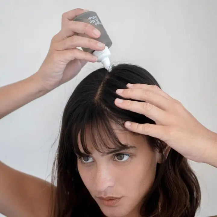 Woman applying Act + Acre Cold Processed Scalp Detox to her roots, massaging the formula into her scalp for deep cleansing and hydration.