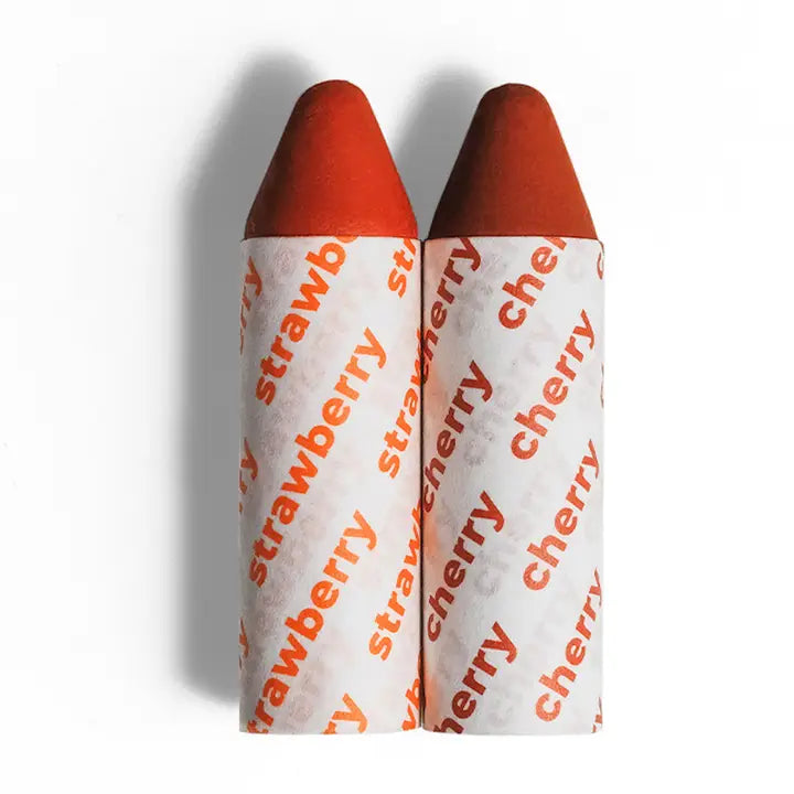 Two Axiology Balmies in Strawberry and Cherry shades, showing their plastic-free, compostable packaging and creamy, blendable formula.